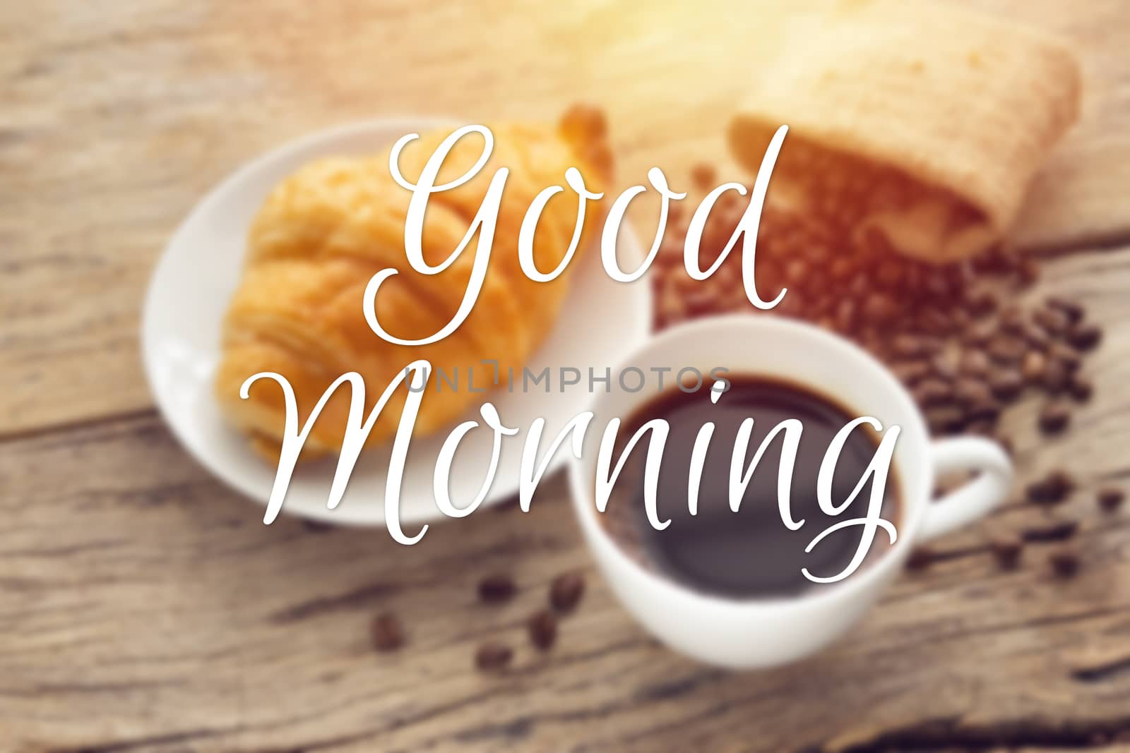 text good morning with blurry of continental breakfast with fresh croissant and hot coffee on wooden table, decoration with coffee bean as background