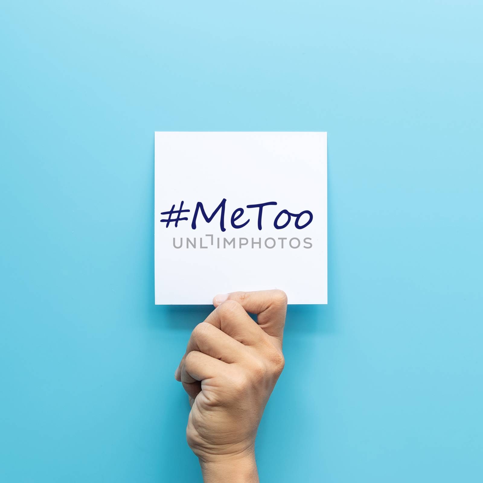 hashtag #MeToo on white paper in hand isolated on blue background. #MeToo is a campaign for movement against sexual harassment and sexual assault. by asiandelight