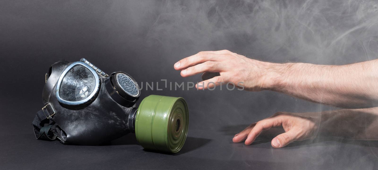 Man in room filled with smoke, trying to reach for vintage gasmask - Isolated on black - Green filter