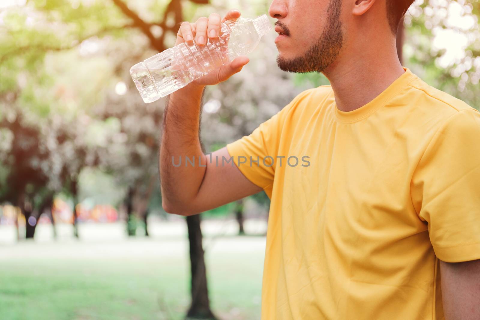 Young asian man jogger drinking water from the bottle after hard exercise in the garden, healthy concept