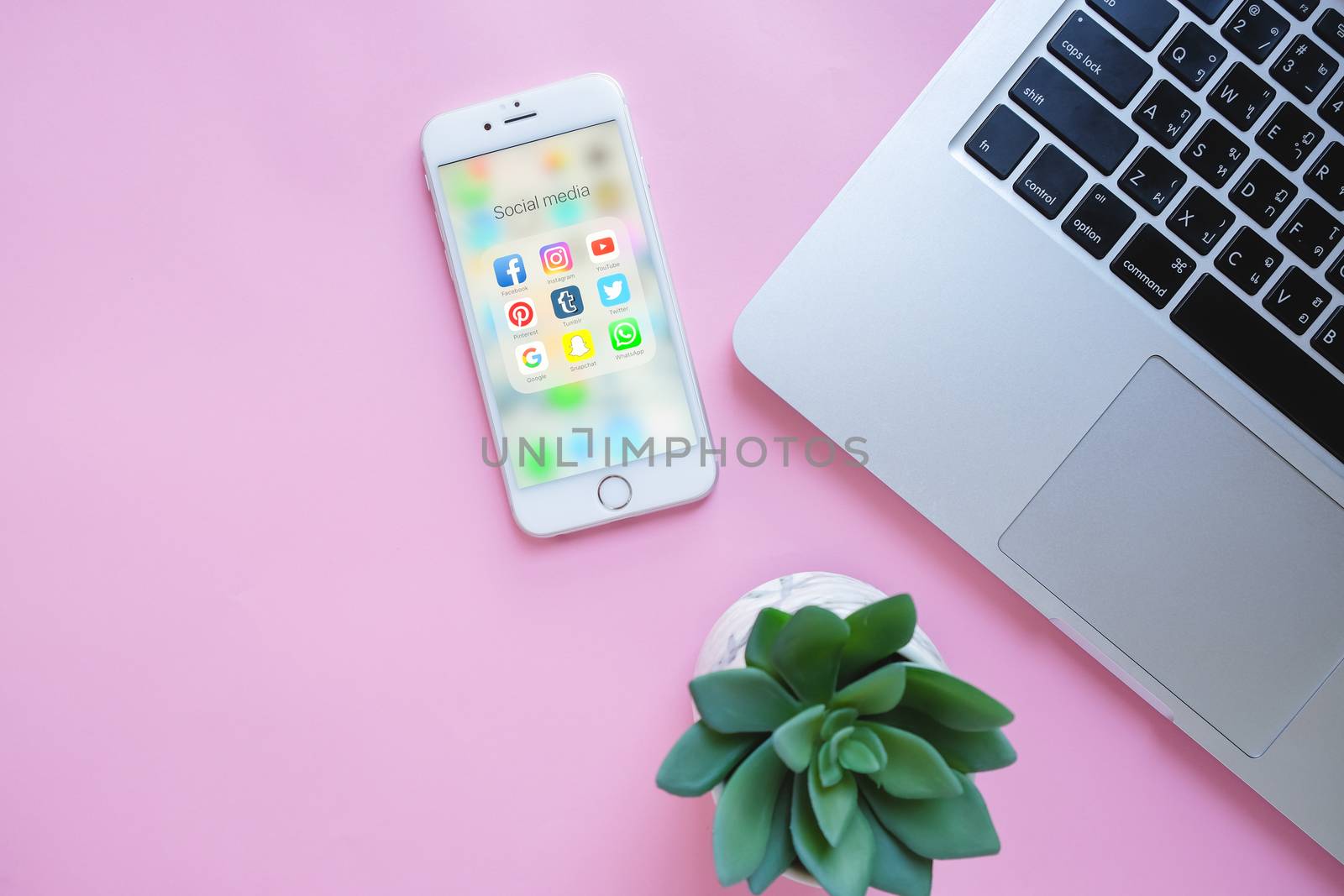 BANGKOK, THAILAND - NOVEMBER 28, 2016:  Group of Popular Social networks icons showing on Apple iPhone 6s screen with laptop and green plant on pink background, Social media are most popular tool for communication.