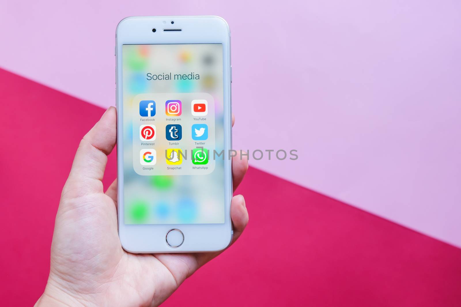 BANGKOK, THAILAND - NOVEMBER 28, 2016:  Hand holding Apple iPhone 6s screen showing group of popular social networks icons on pink and red background, Social media are most popular tool for communication.