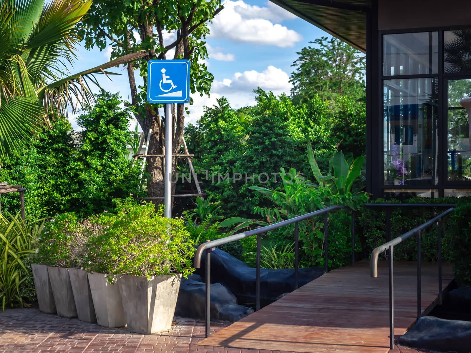 Disabled way sign in front of cafe on green nature landscape background. Wheelchair ramp way with disabled sign for support wheelchair disabled people.