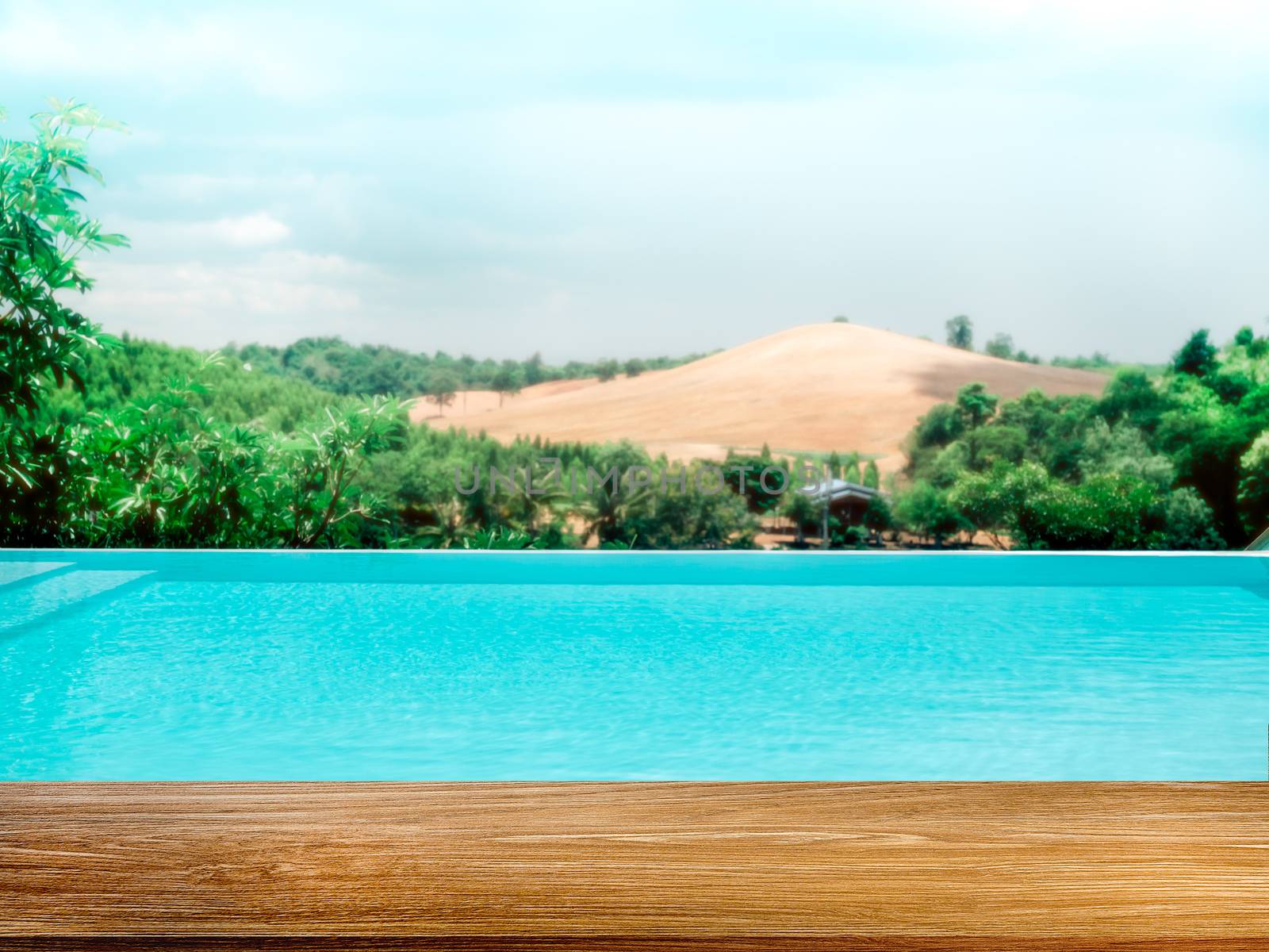 Empty top table wood plank with blurred swimming pool and mountain view on blue sky background.