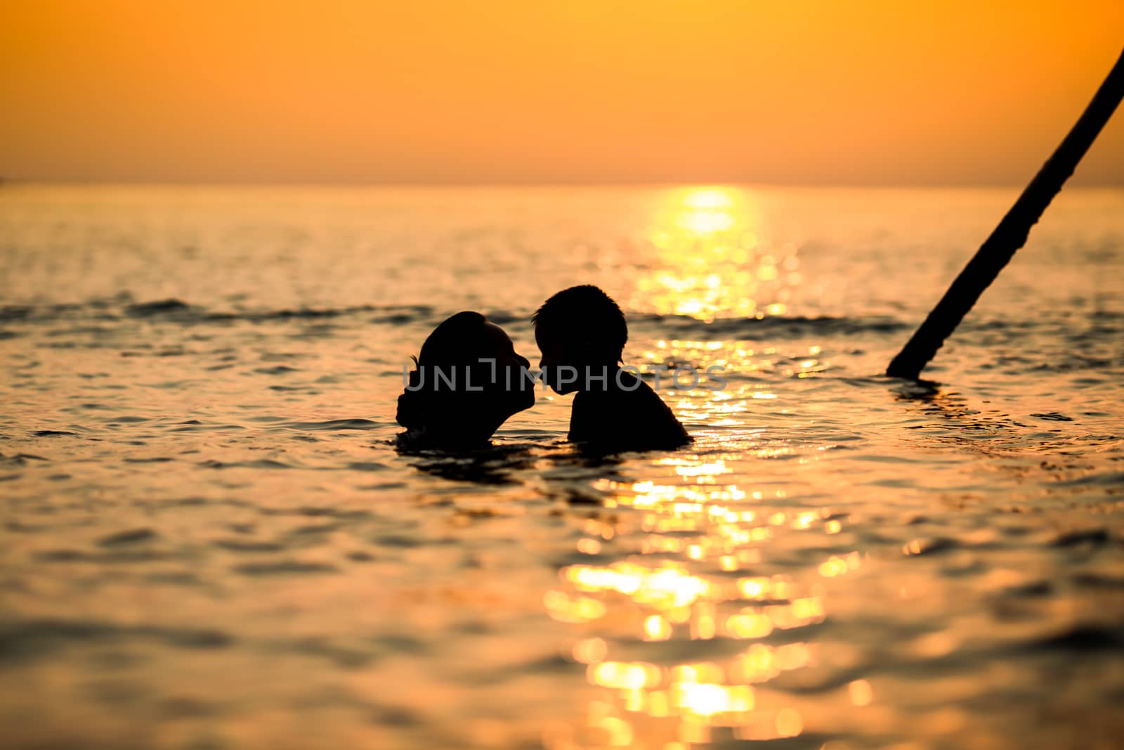 Silhouette mother and child are kissing in the sea while the sunset.