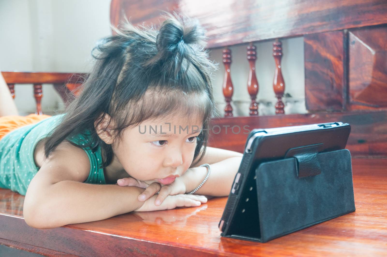 Unhappy Young Girl lying on wooden stool and Learning online course on Wireless Digital Tablet while staying at home in situation of Corona Virus or Covid 19 outbreak.