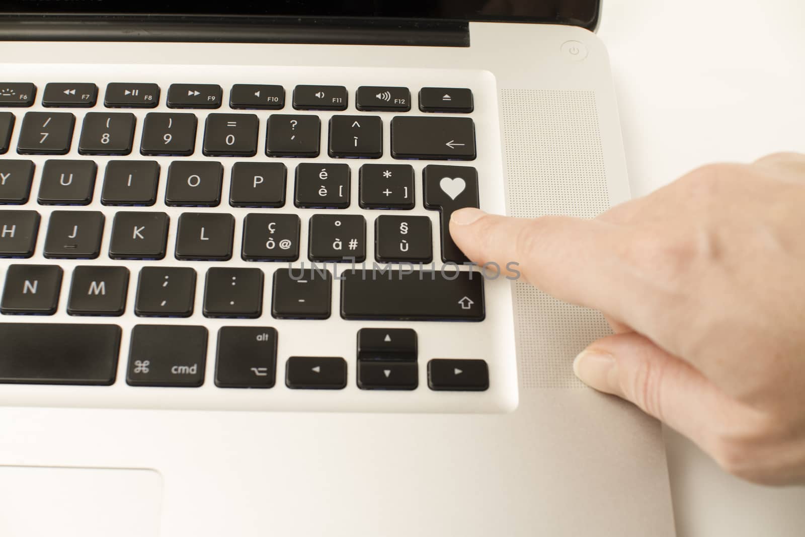 Technology also applies to emotional relationships: a woman's hand is about to press a key on a laptop keyboard with a stamped heart
