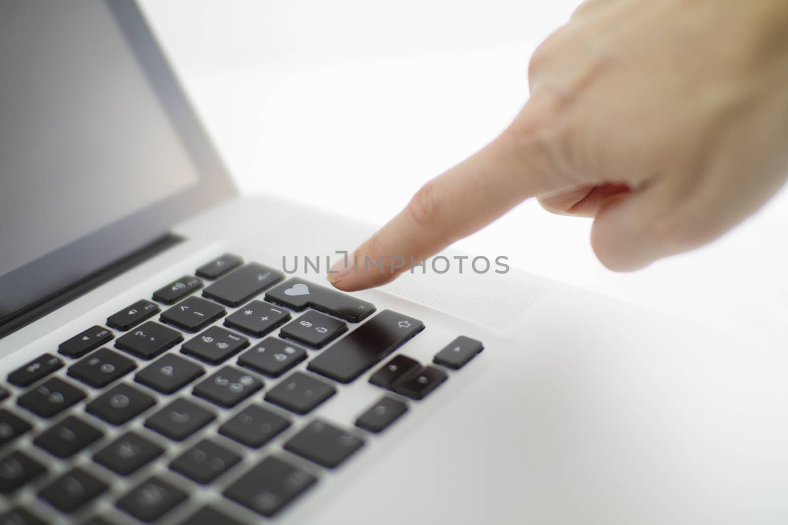 Technology also applies to emotional relationships: a woman's hand is about to press a key on a laptop keyboard with a stamped heart