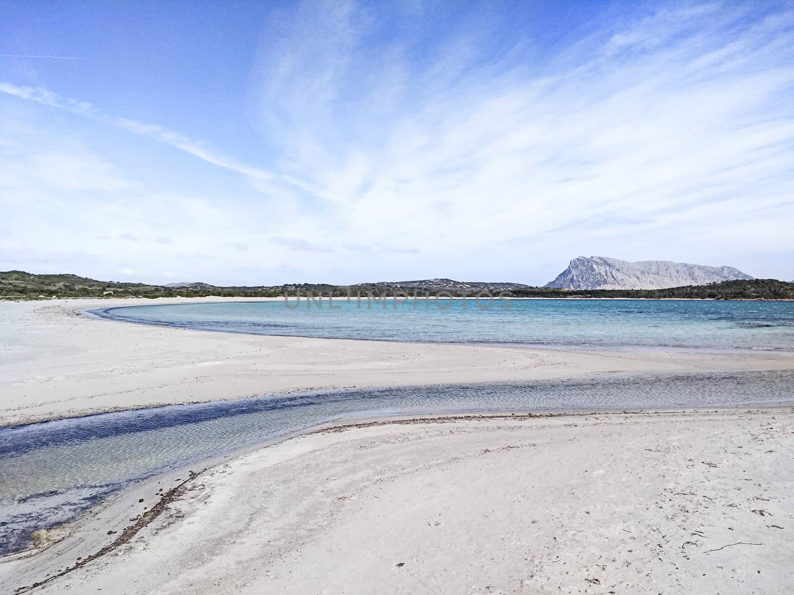 Beautiful deserted white beach in Sardinia, Lu Impostu, with sea in various shades of blue, curves of sand marked by water and the island of Tavolara in the background with blue sky