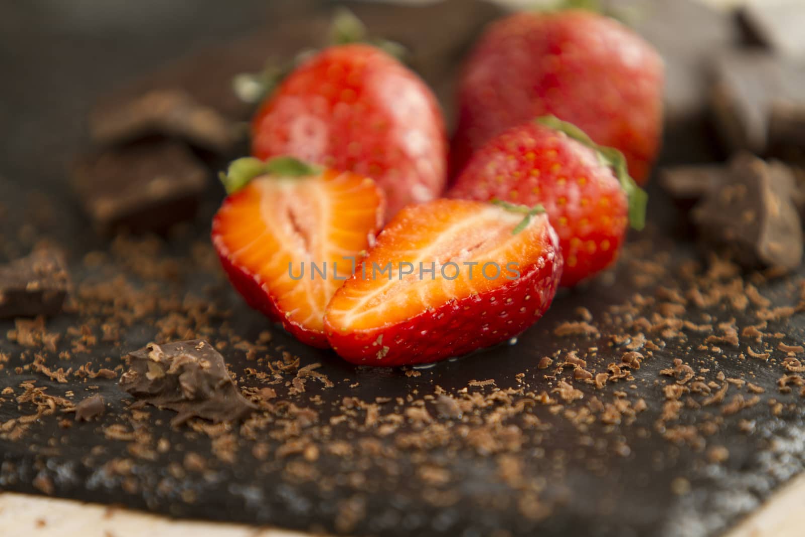 Neatly placed strawberries on a slate plate with chopped chocolate and grated around on a light wooden background and selective focus