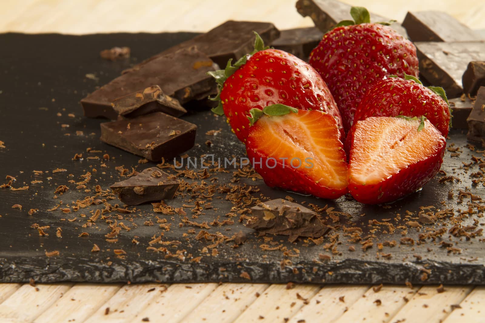 Neatly placed strawberries on a slate plate with chopped chocolate and grated around on a light wooden background and selective focus