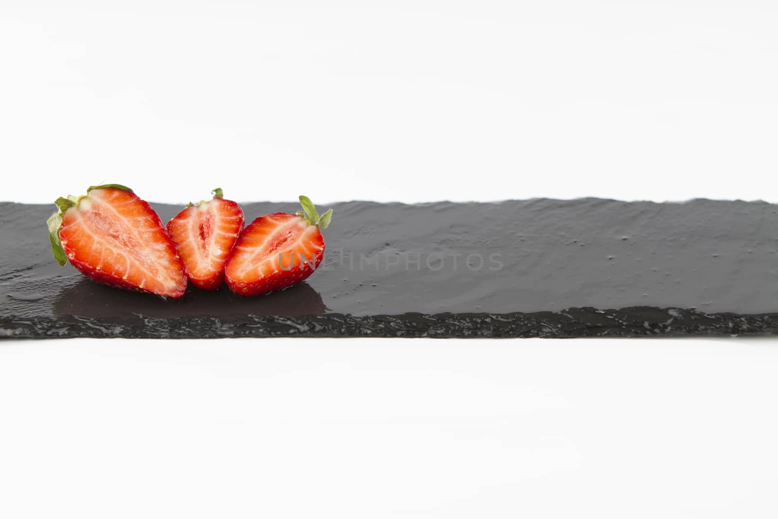 Close-up of three isolated strawberries on a rectangular strip of wet slate on a white background shot in high angle view with selective focus