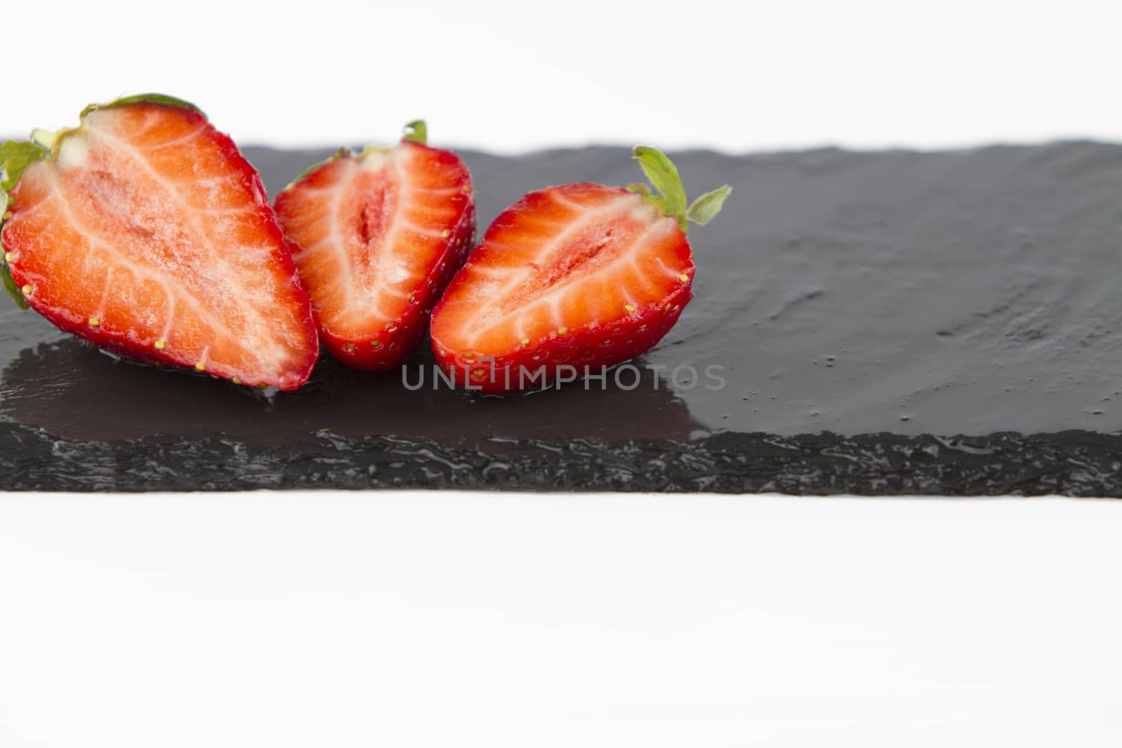Close-up of three isolated strawberries on a rectangular strip of wet slate on a white background shot in high angle view with selective focus