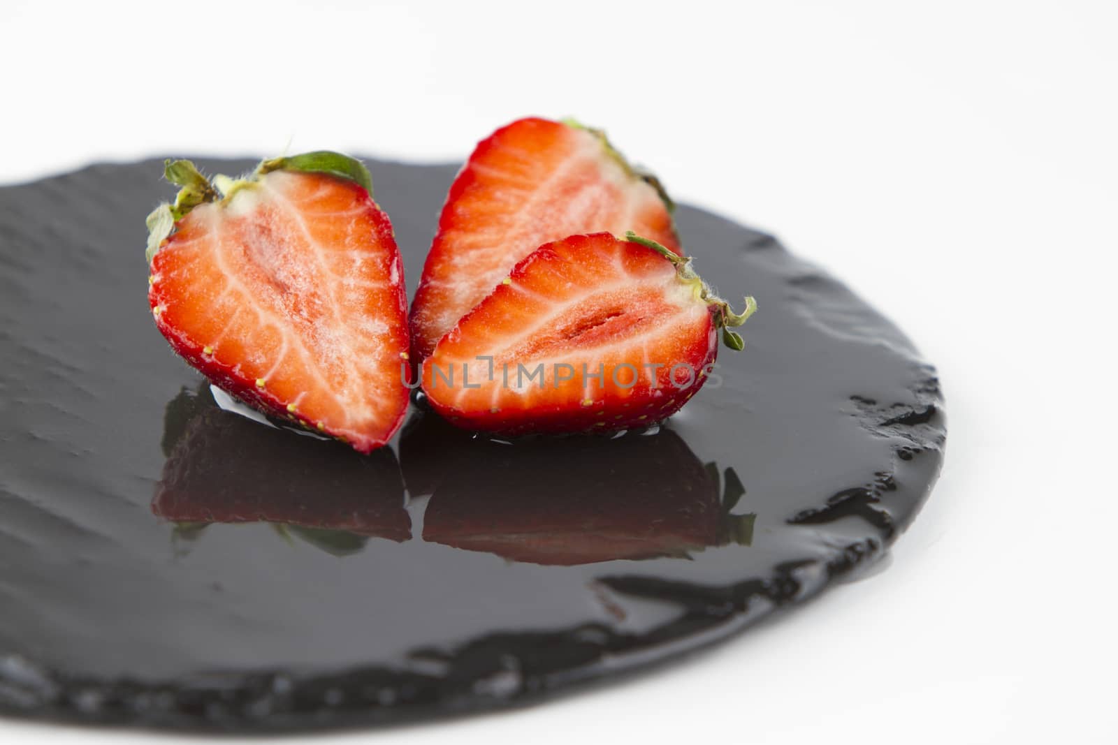 Close-up of three strawberries isolated on a wet round slate plate on a white background shot in high angle view with selective focus