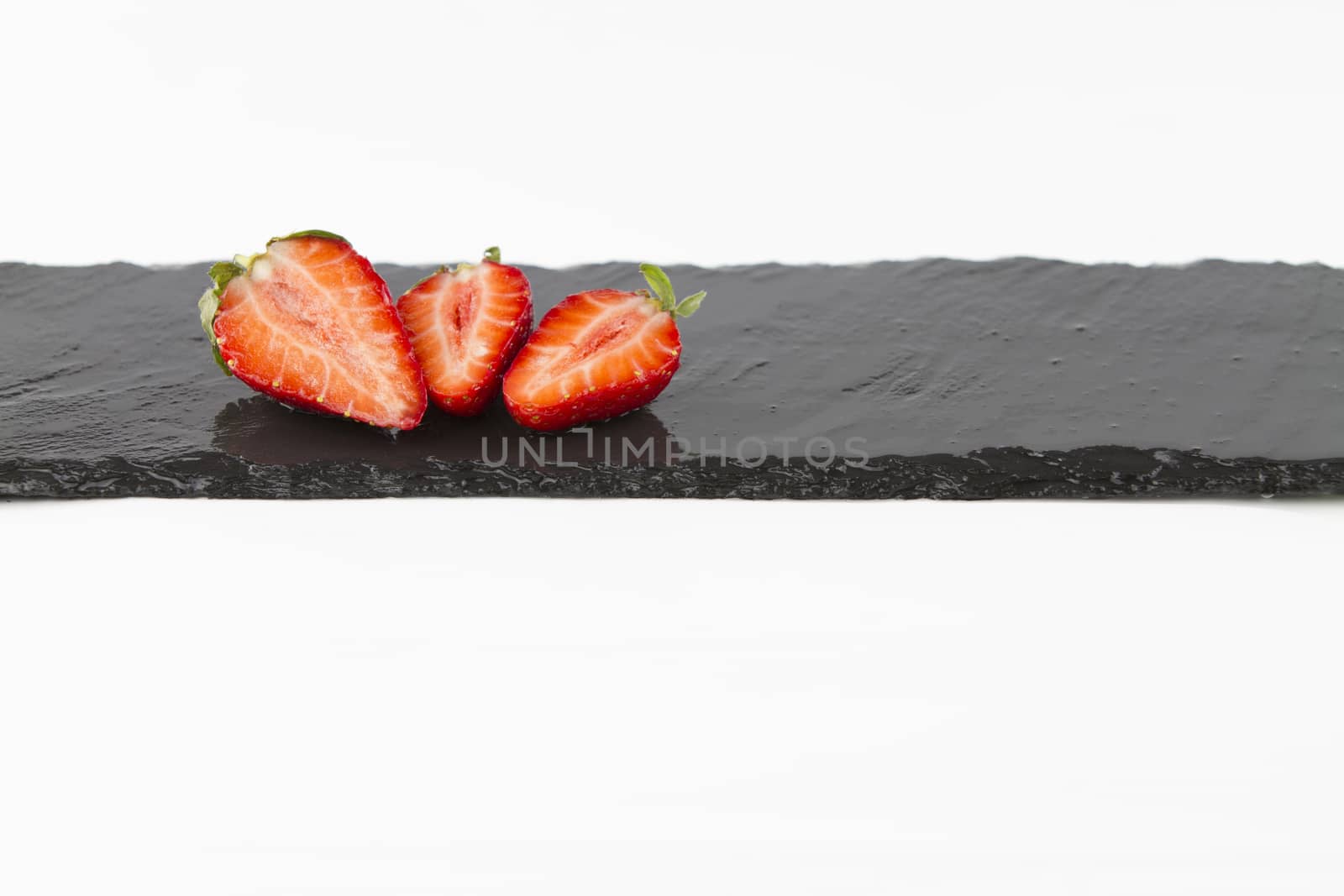 Close-up of three isolated strawberries on a rectangular strip of wet slate on a white background shot in high angle view with selective focus