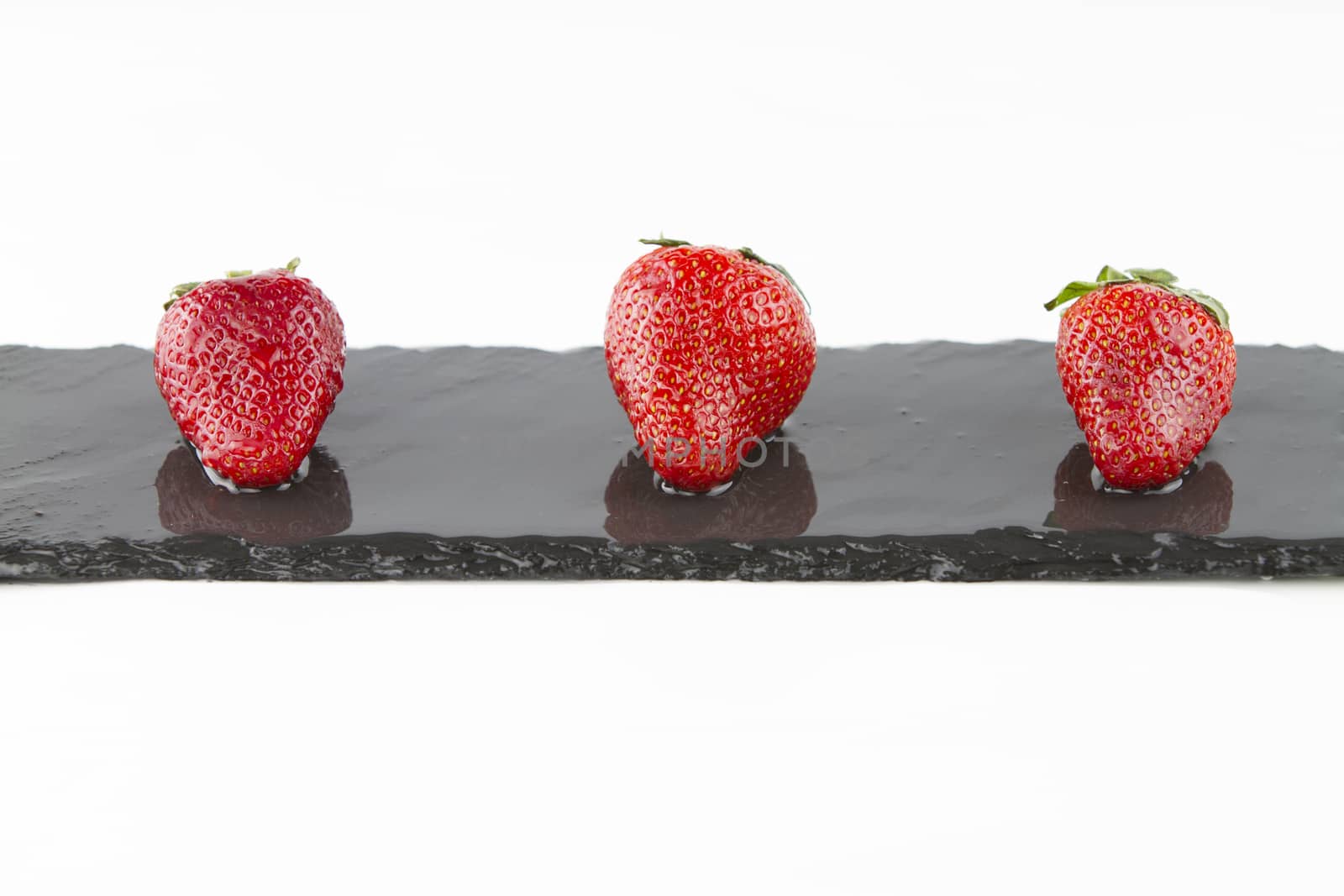 Close-up of three isolated strawberries on a rectangular strip of wet slate on a white background shot in high angle view with selective focus