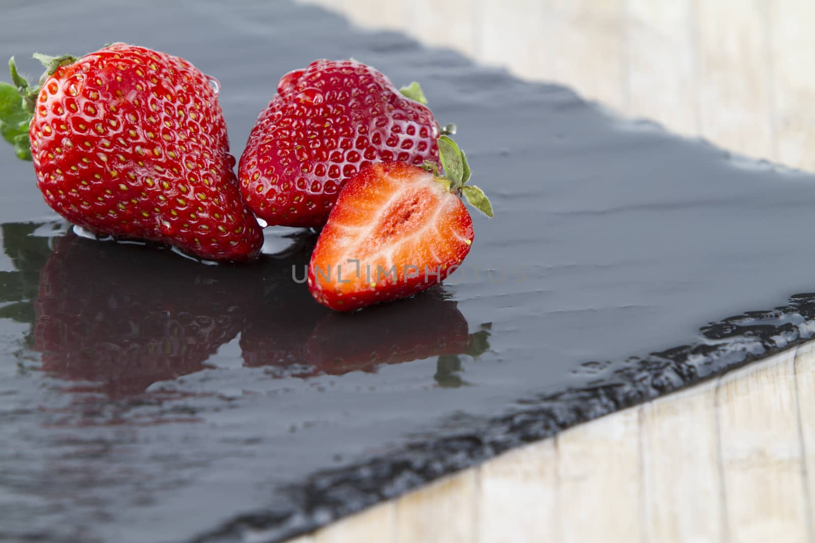 Close-up of three strawberries isolated on a wet square slate plate on a white background shot in high angle view with selective focus