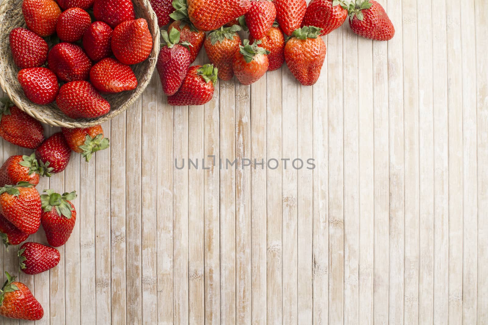 Strawberries copy space with a small basket of strawberries in the upper left corner surrounded by strawberries scattered on a wooden background taken from above