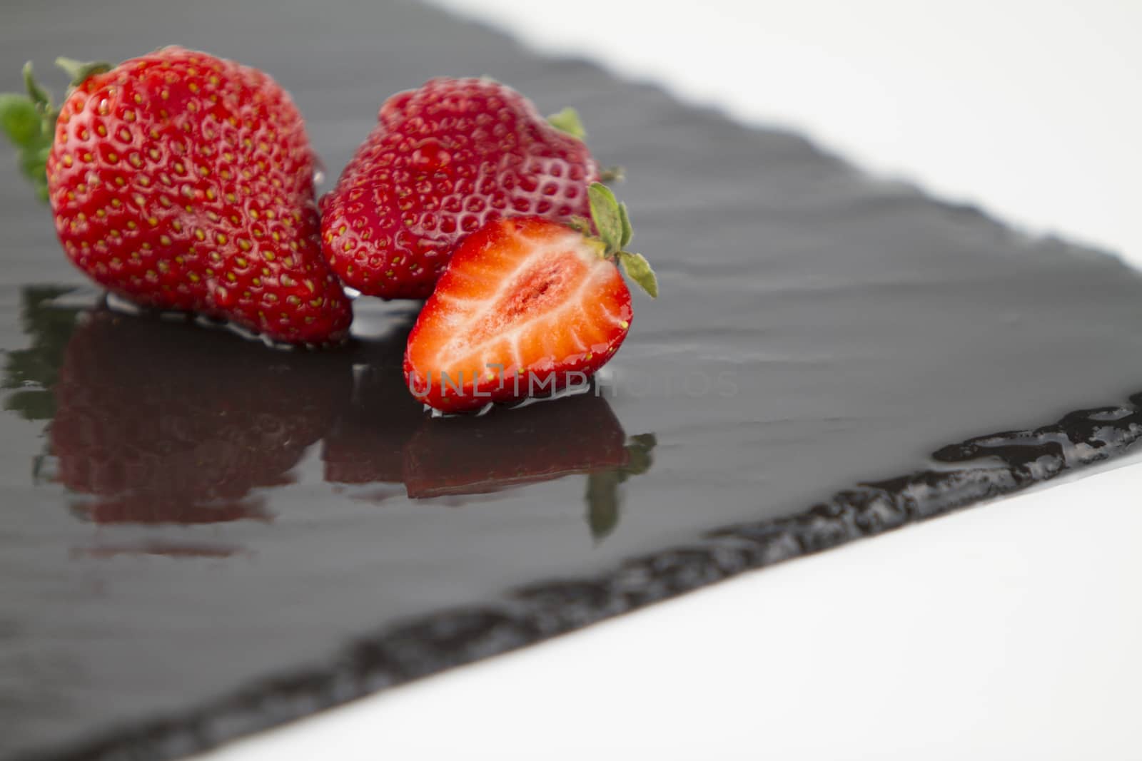 Close-up of three strawberries isolated on a wet square slate pl by robbyfontanesi