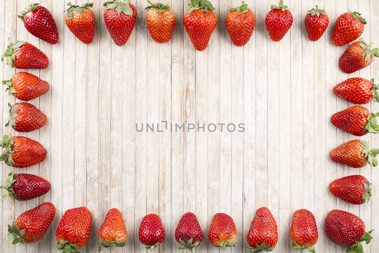 Strawberries copy space with strawberries all along the perimeter to form a rectangle on a background of light wood taken from above