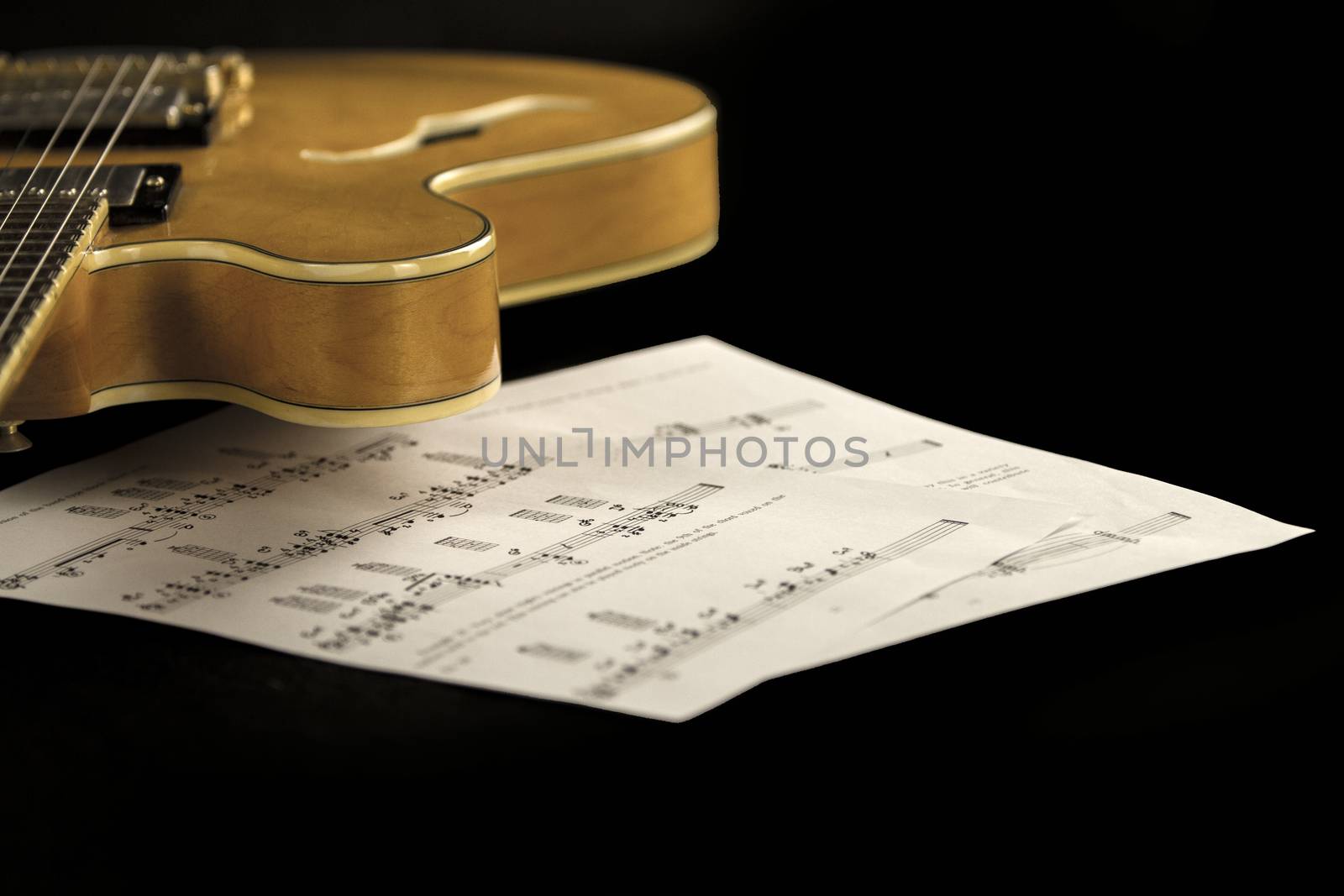 Vintage archtop guitar in natural maple close-up high angle view with music sheets on black background