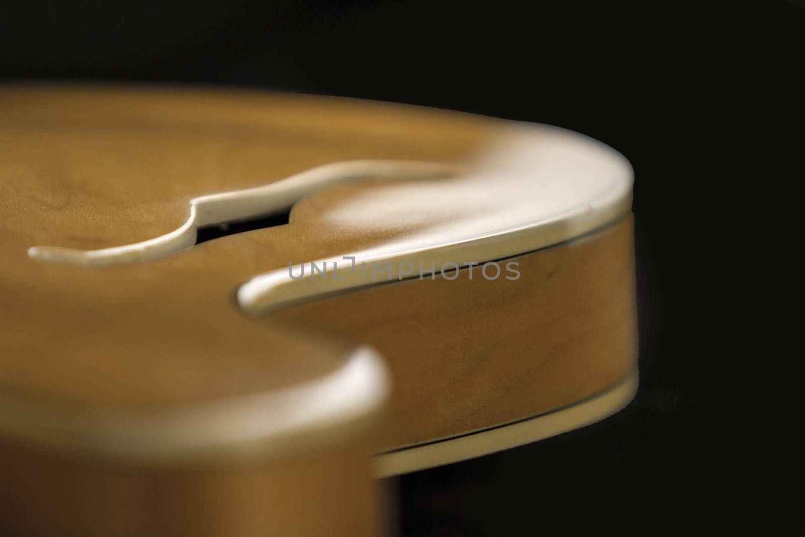 Vintage archtop guitar in natural maple close-up high angle view with F-hole detail in selective focus and black background