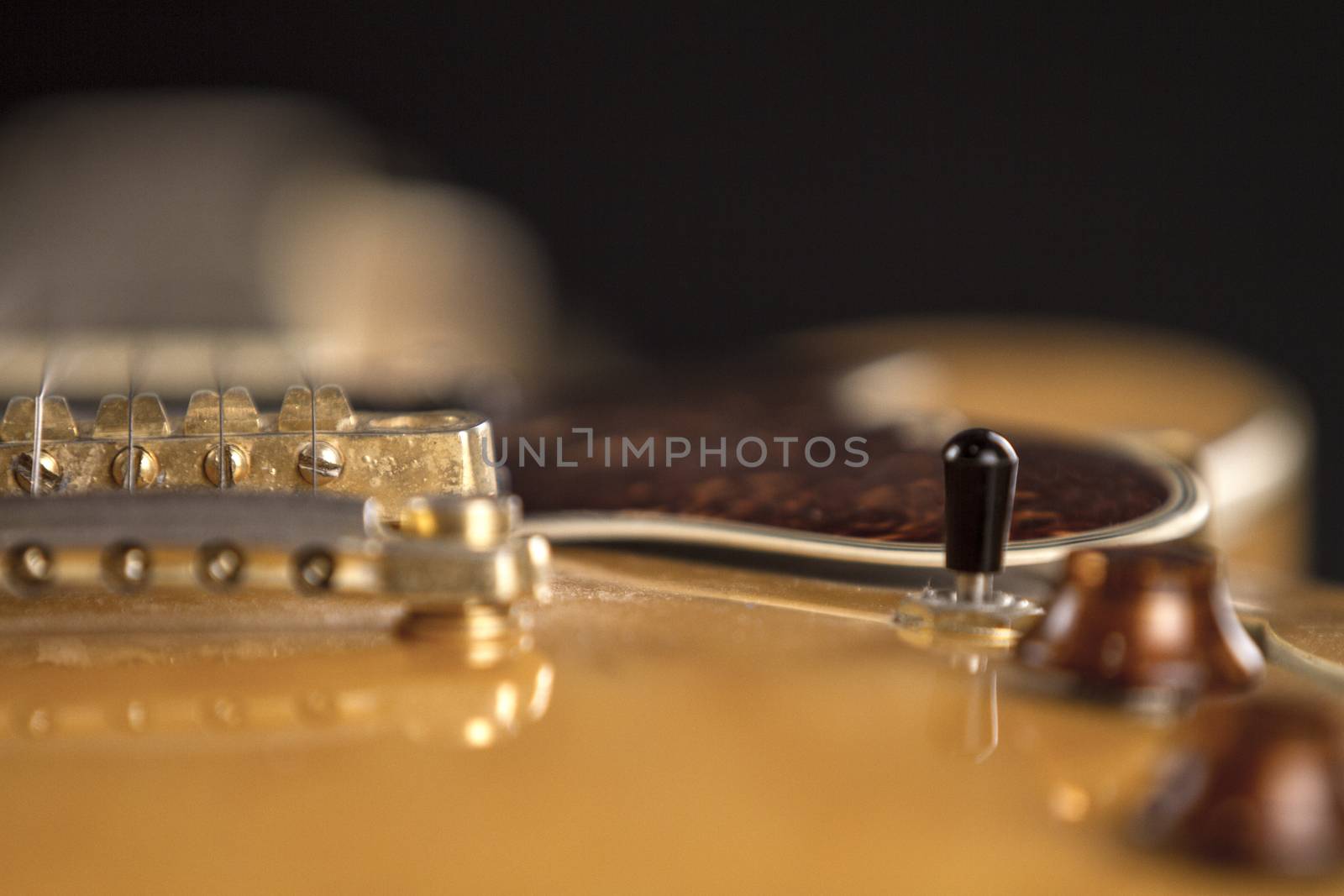 Vintage archtop guitar in natural maple close-up high angle view on black background, golden bridge, volume and tone controls detail in selective focus