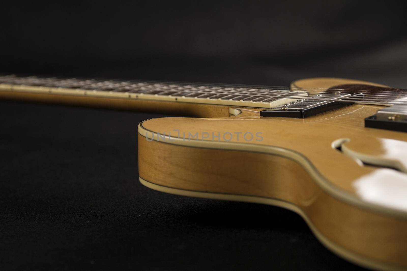 Vintage archtop guitar in natural maple close-up high angle side view in selective focus on black background