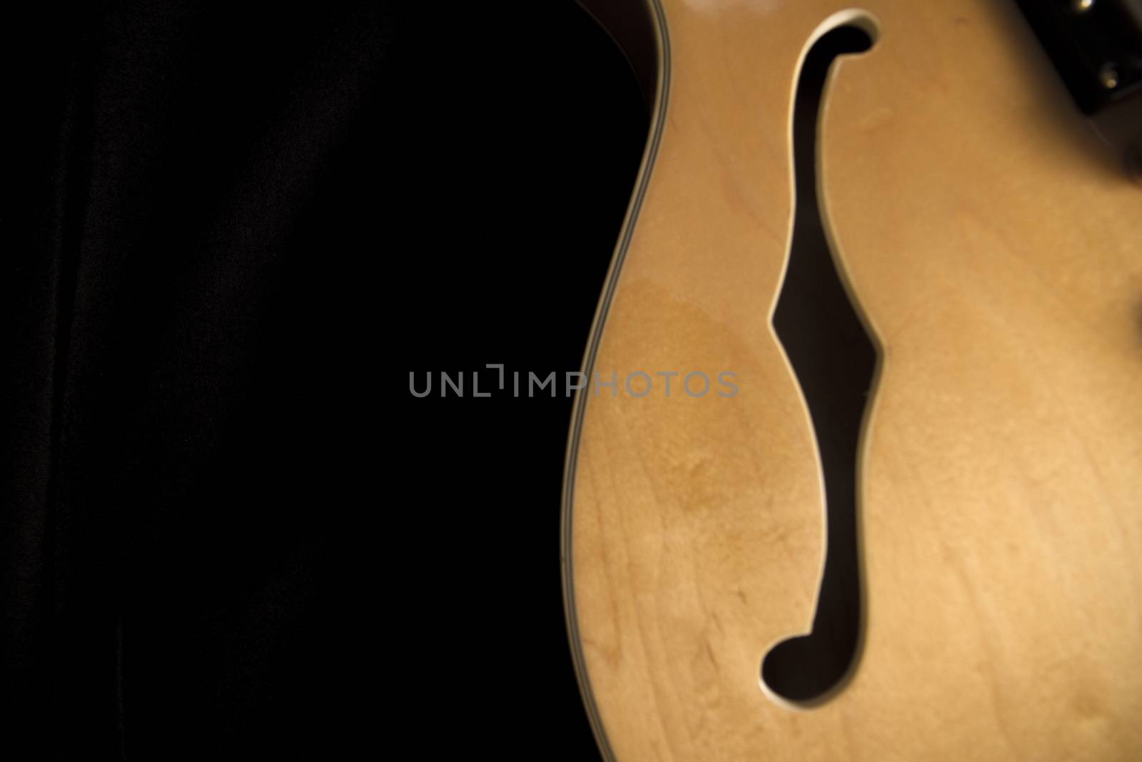 Vintage archtop guitar in natural maple close-up from above on black background, F-hole detail