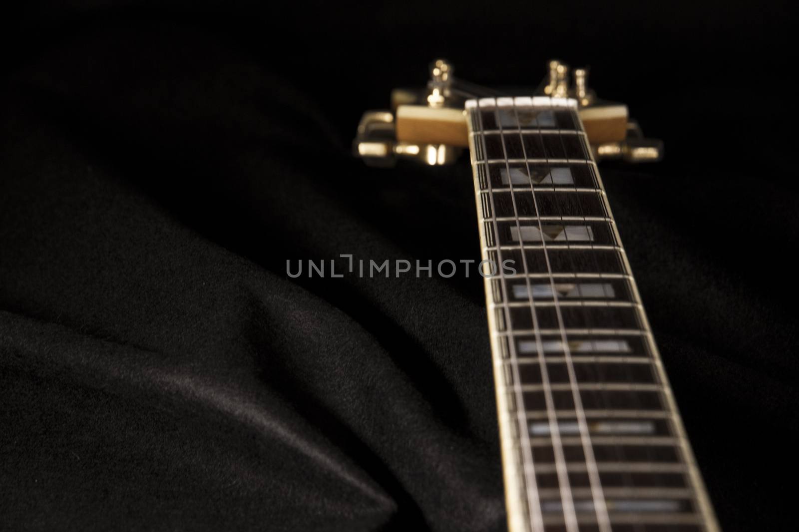 Vintage archtop guitar in natural maple close-up high angle view on black background, rosewood fingerboard with frets and fret markers detail in selective focus