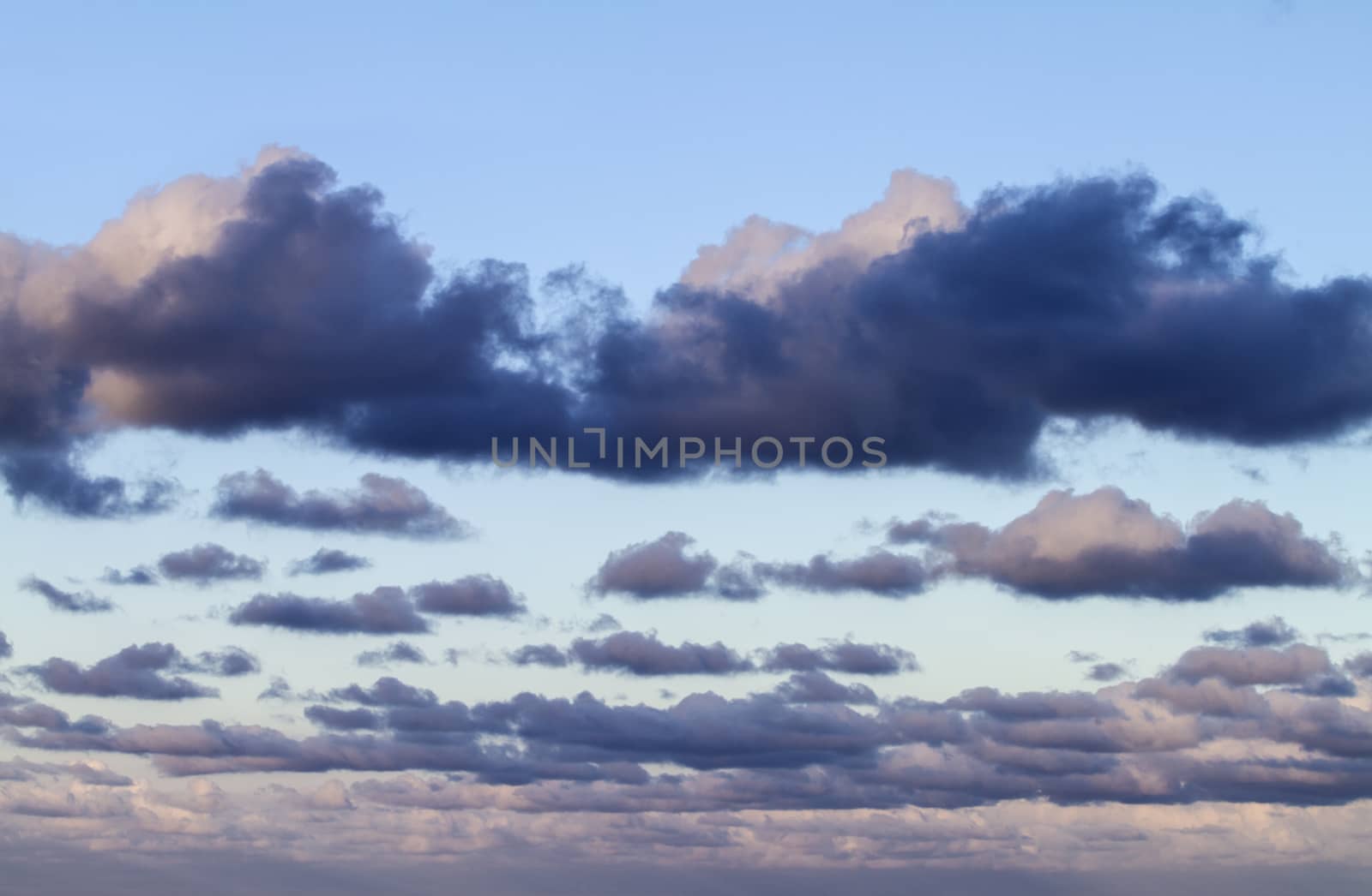 Impressive sky at sunset with layers of clouds tinged with pink that slope down towards the horizon