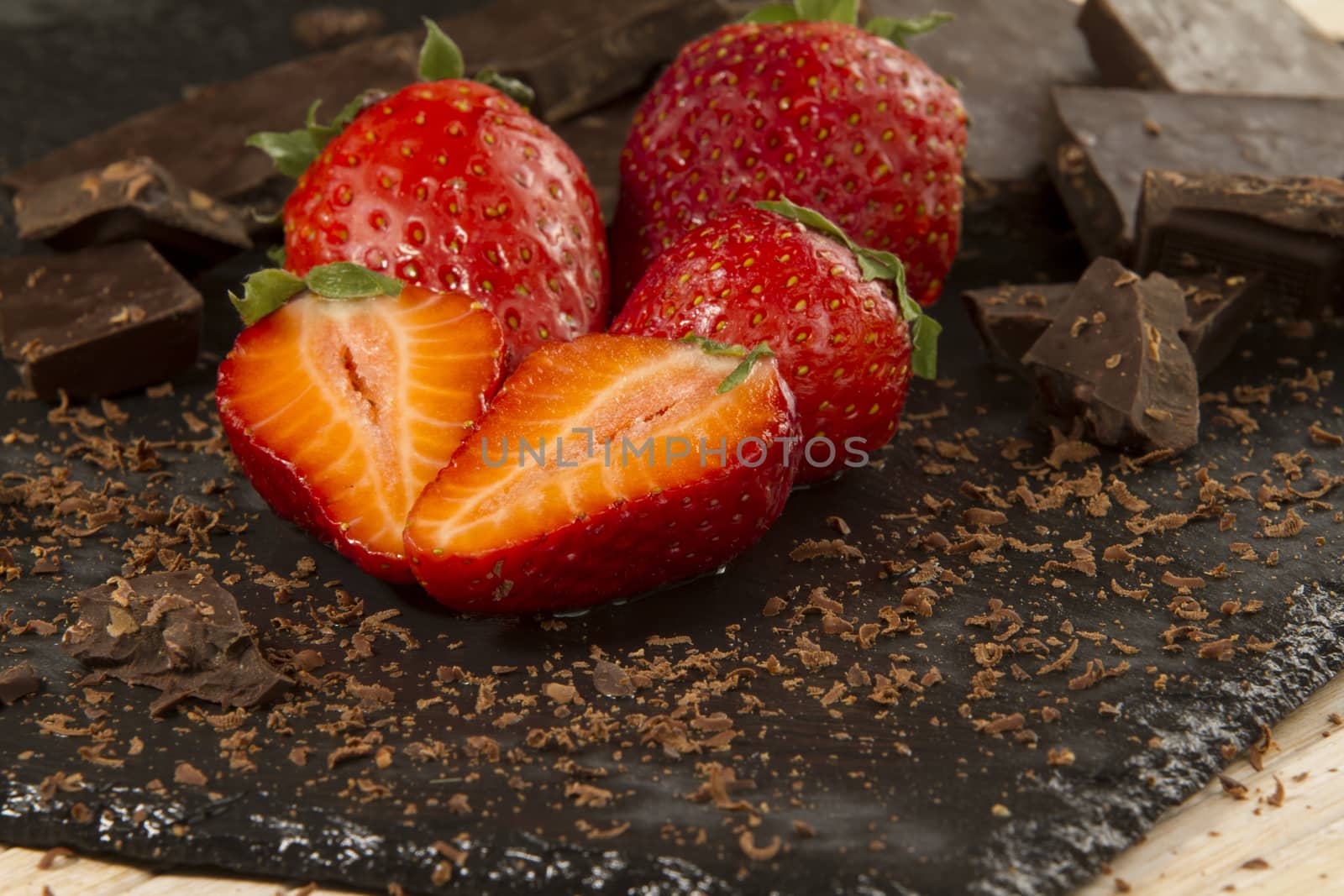 Neatly placed strawberries on a slate plate with chopped chocolate and grated around on a light wooden background and selective focus