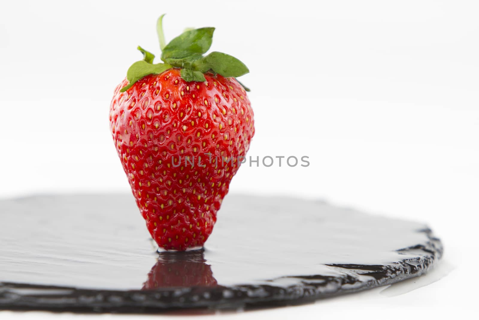 Close-up of a strawberries isolated on a wet round slate plate o by robbyfontanesi