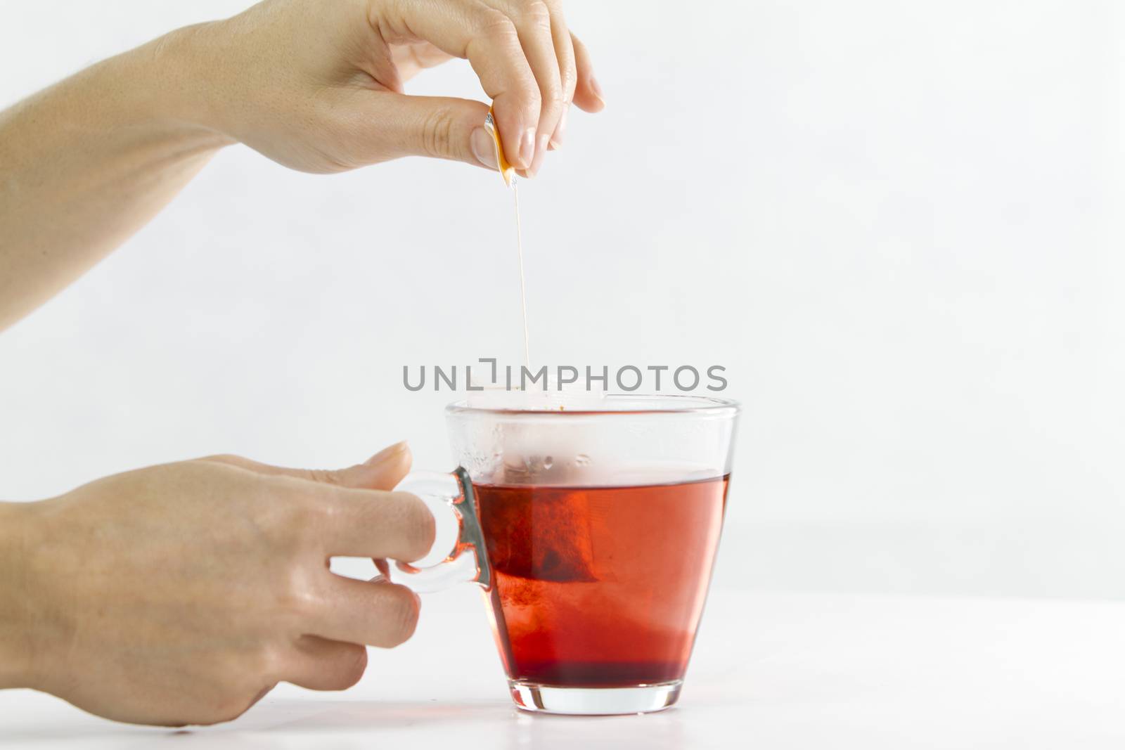 Close-up of a woman hand dipping a sachet of Hibiscus Tea in a g by robbyfontanesi