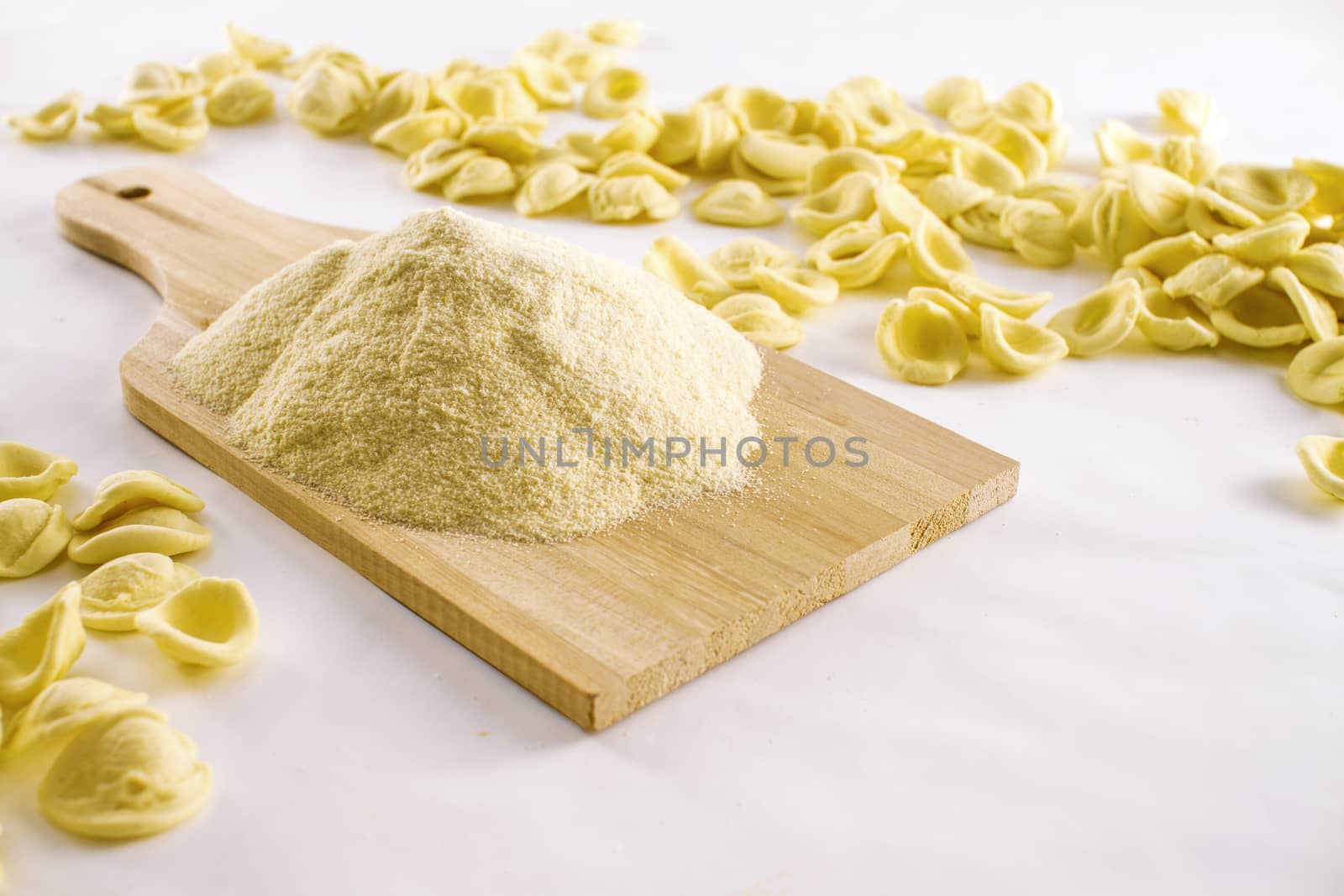 Close-up of orecchiette of typical italian handmade pasta with a pile of durum wheat flour on wooden cutting board