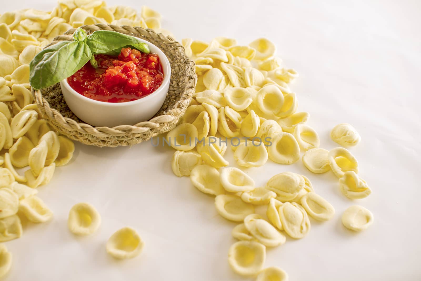 Close up still life of italian handmade pasta orecchiette pugliesi with tomato puree and basil on white background