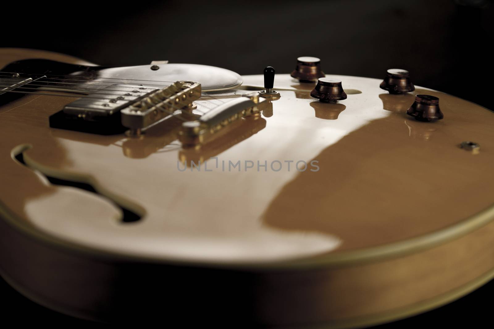 Vintage archtop guitar in natural maple close-up high angle view on black background, controls detail in selective focus
