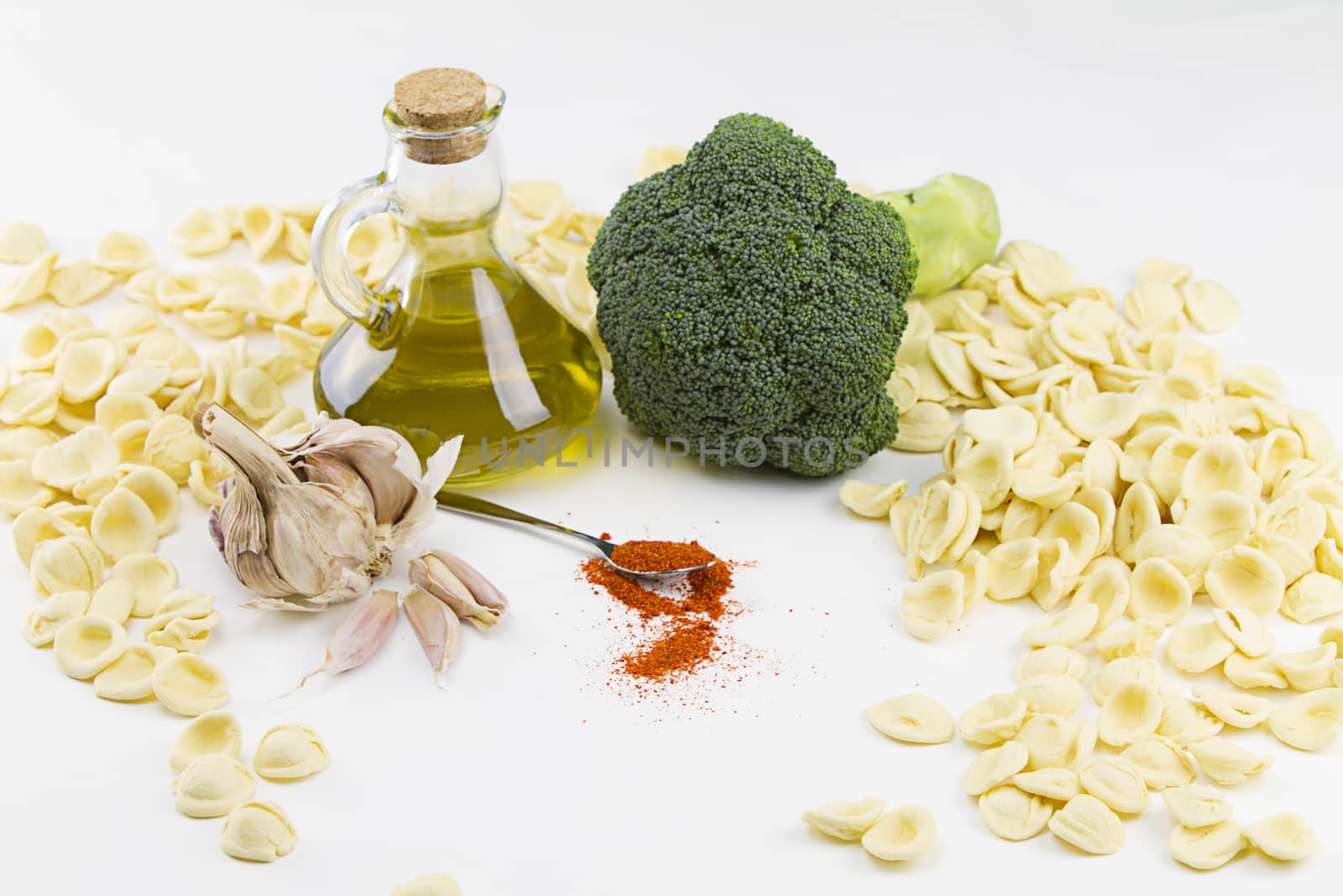 Close-up o f ingredients of typical italian recipe orecchiette ai broccoli: handmade durum wheat flour pasta orecchiette, broccoli, extra virgin olive oil, garlic and ground chili on white background