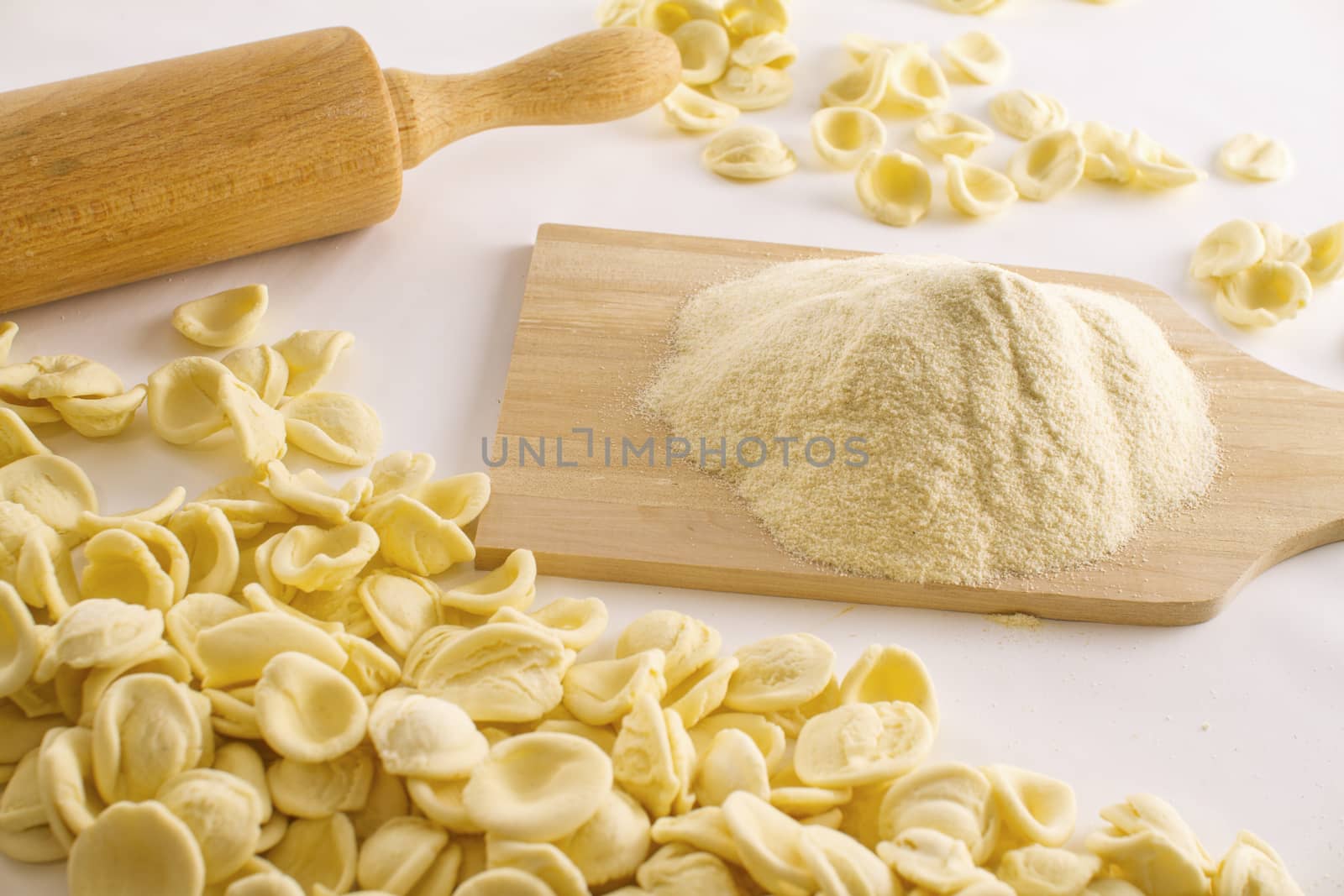 Close-up of orecchiette of typical italian handmade pasta with a pile of durum wheat flour on wooden cutting board