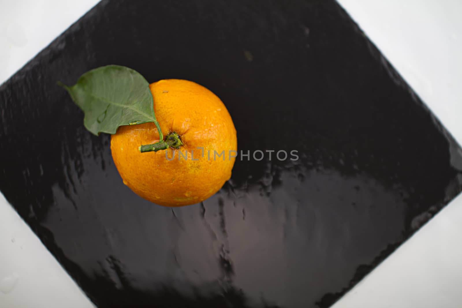 Orange with leaf shot from above on a square black  wet slate plate with reflected light effects