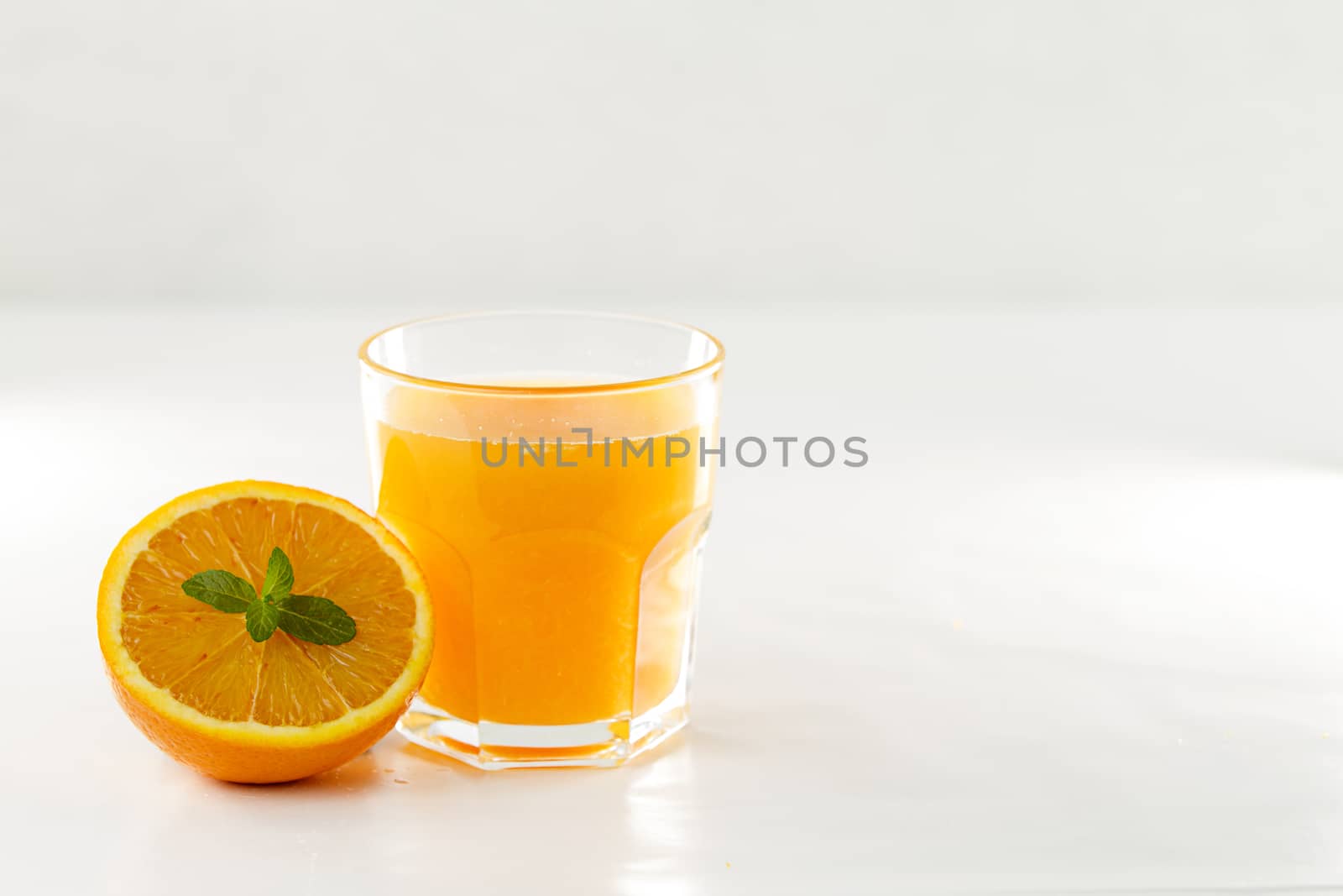 An inviting glass full of orange juice and a half one with a fresh mint leaf in its center on a white background