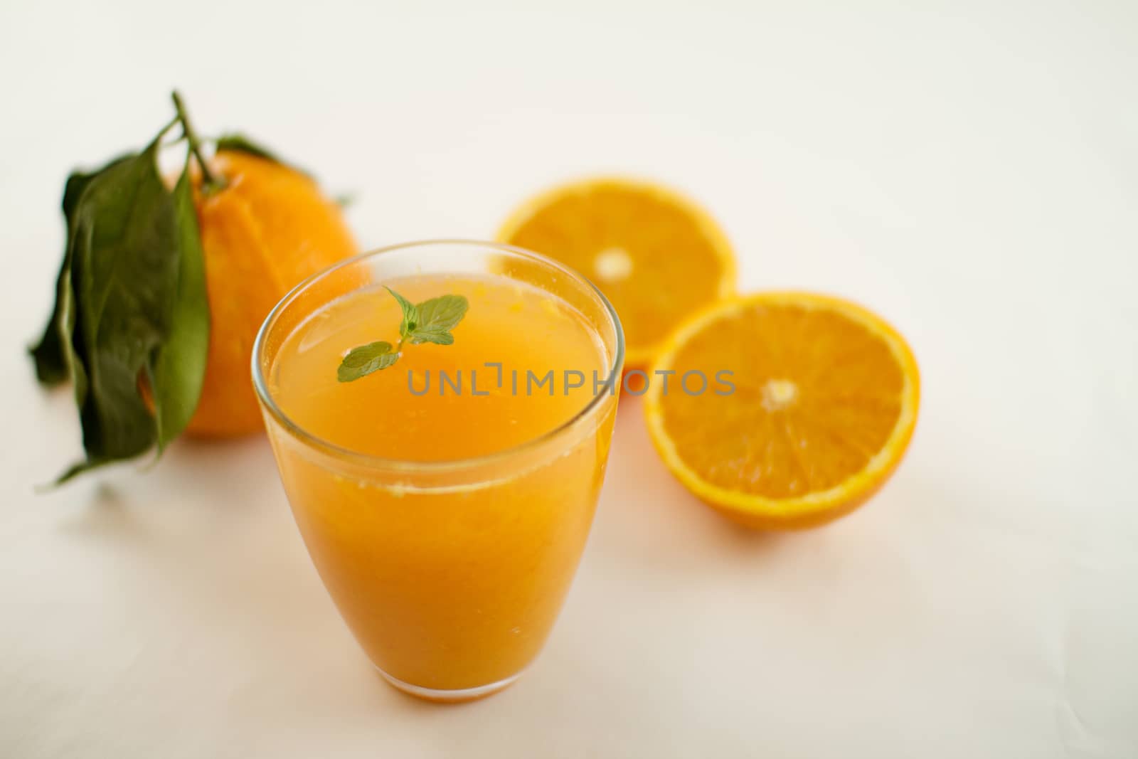 An inviting glass full of orange juice with a fresh mint leaf th by robbyfontanesi
