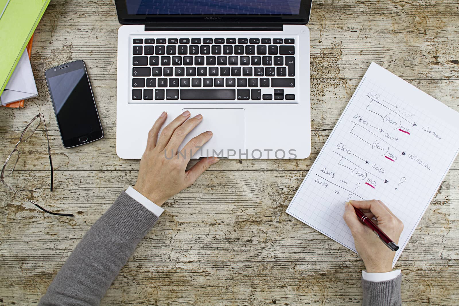 Business woman shooting from above working on laptop on wooden table with while taking notes on a notepad