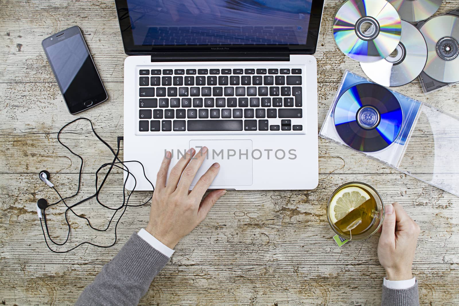 Young woman shooting from above working on laptop on wooden table listening to music cd with a cup of tea and headphone