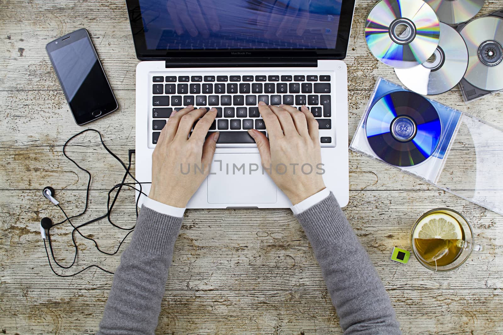 Young woman shooting from above working on laptop on wooden table listening to music cd with a cup of tea and headphone