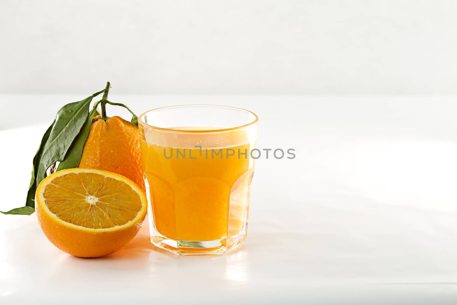 An inviting glass full of orange juice, a orange divided in two and a whole one with leaf on a white background
