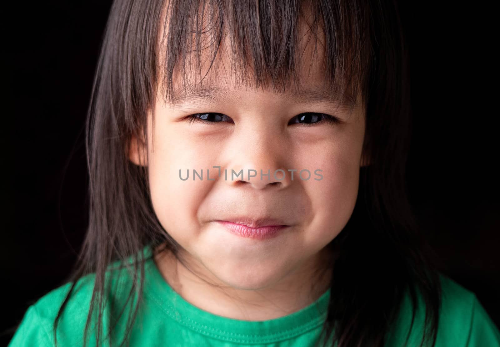 Portrait face of Asian little child girl with happy expression on dark background.