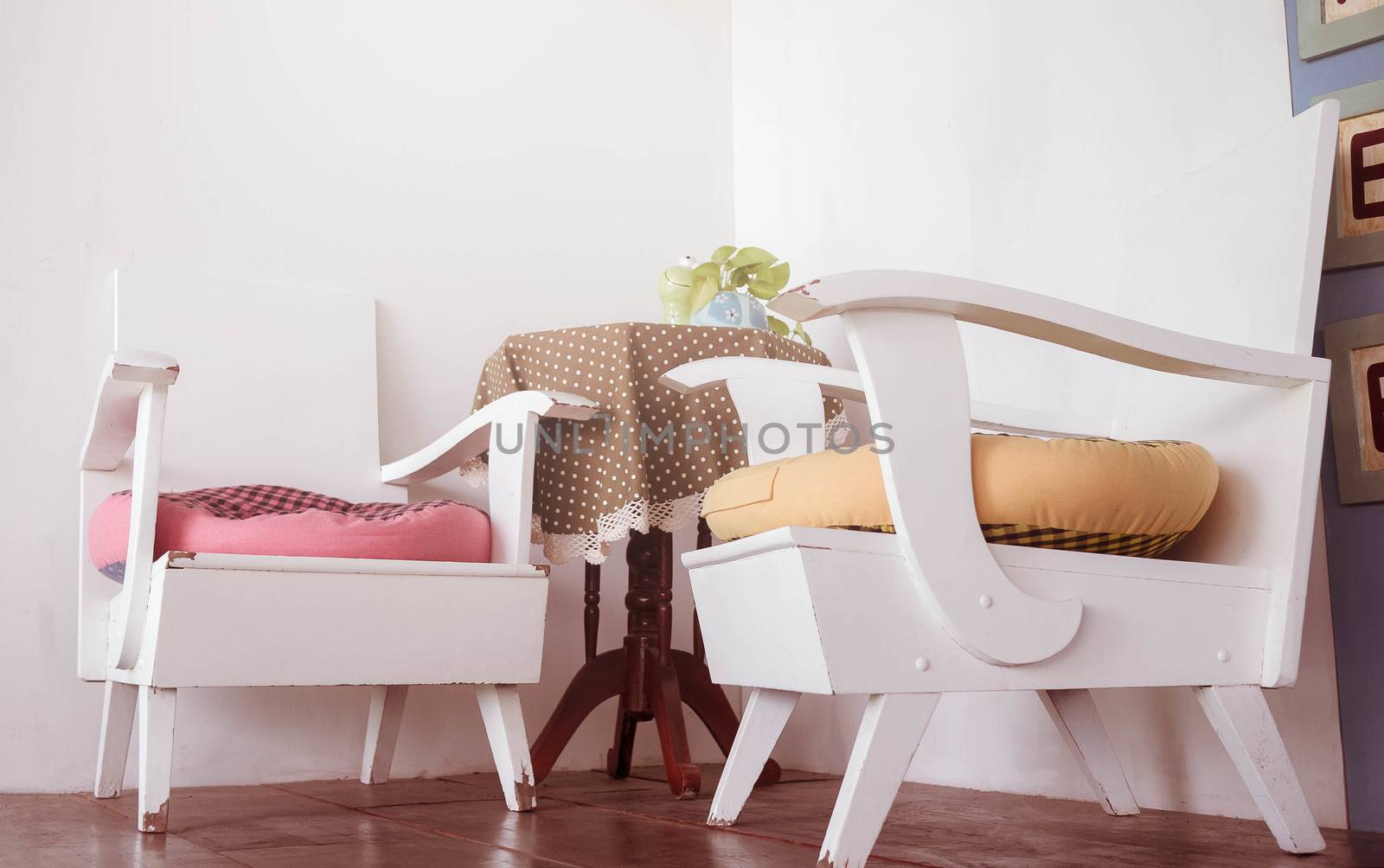 White wooden chairs and wooden table with beautiful color table covers and cute small flower vase in the living corner at the cafe. Relaxation corner decoration idea.