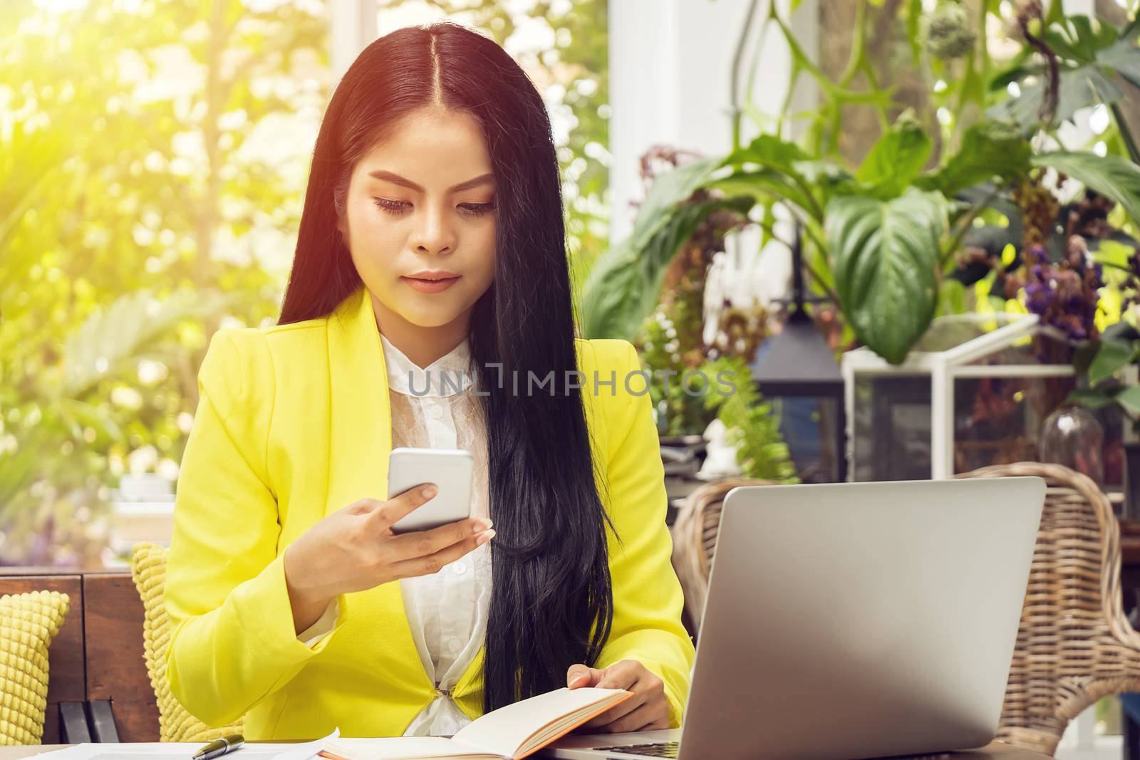 portrait of beautiful and confident Asian business woman sitting in front of notebook laptop and checking on phone for update appointment at workplace. by asiandelight