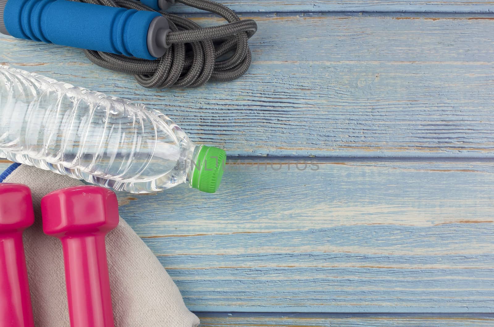 Top or flat lay view of dumbbells, towel, water and skipping rope with copy space area on blue wooden background. Healthy concept. Selective focus.